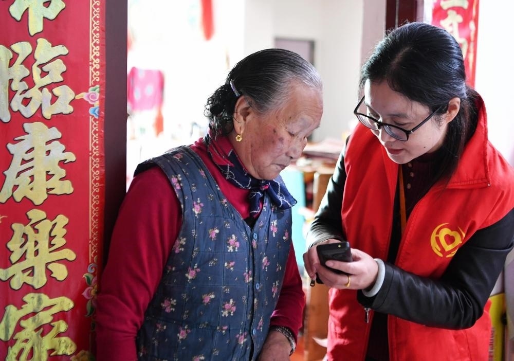 在福州市長(zhǎng)樂區(qū)航城街道籌岐村，智慧養(yǎng)老平臺(tái)派駐社區(qū)的助老員（右）在為老人陳鳳英（左）講解養(yǎng)老定制手機(jī)的用法（2021年11月26日攝）。新華社記者 魏培全 攝