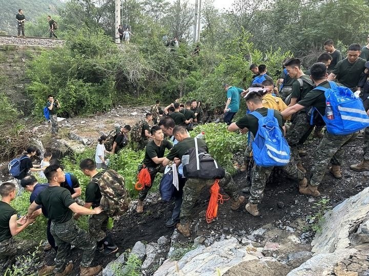 8月2日，Z180次受困列車的旅客在武警北京總隊(duì)機(jī)動(dòng)第三支隊(duì)官兵的幫助下徒步前往轉(zhuǎn)運(yùn)客車（手機(jī)照片）。新華社記者 王艷剛 攝