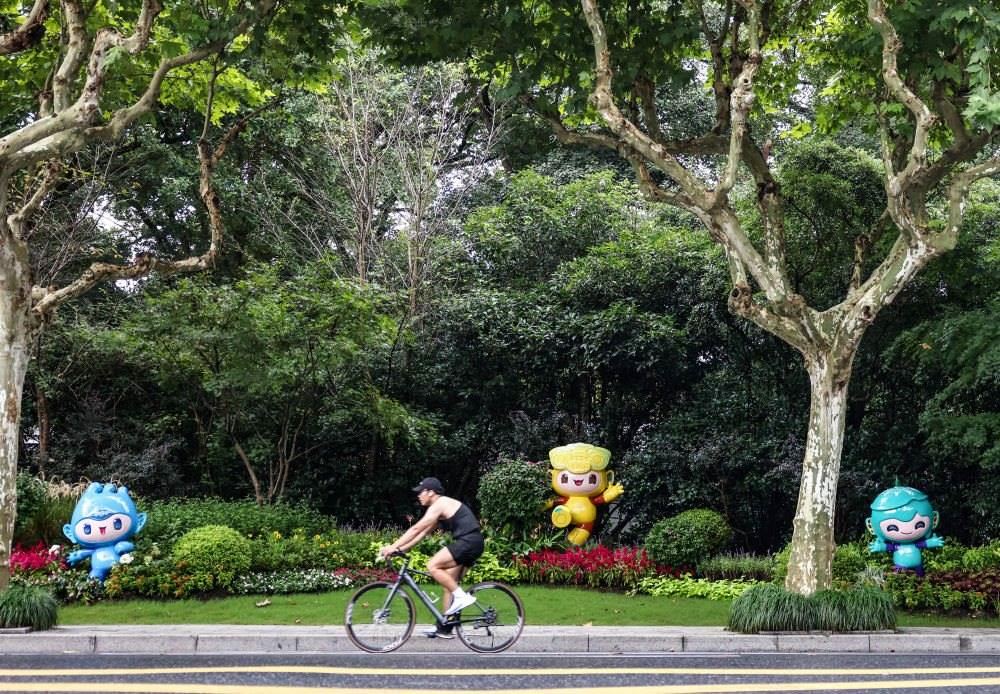 市民在杭州市南山路上一處亞運會主題吉祥物雕塑前騎自行車。