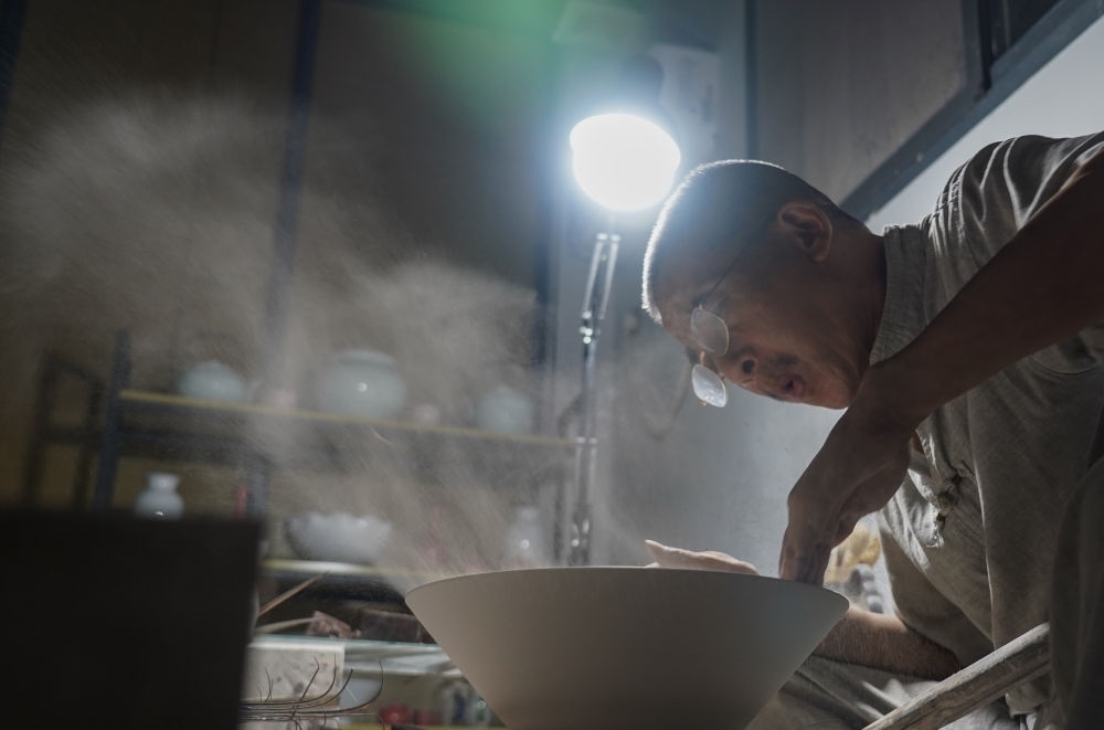 ↑ 在景德鎮(zhèn)，手工匠人吹去坯內(nèi)的泥土（2021年7月14日攝）。