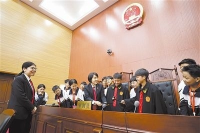 圖③：同學(xué)們穿法袍、敲法槌，爭(zhēng)做“小法官”。
