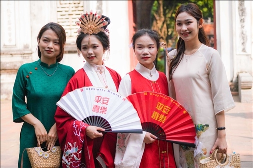 身穿古裝的中國游客和身穿越南傳統(tǒng)服飾奧黛的越南青年在文廟門前合影。