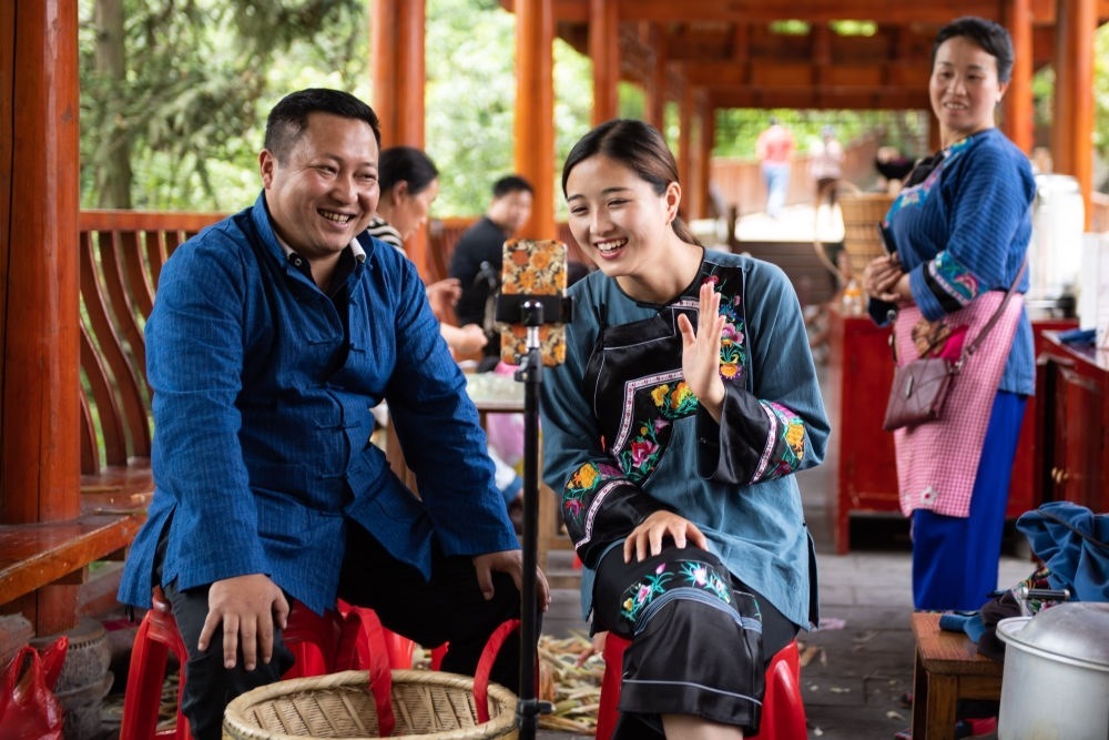 在湖南省湘西土家族苗族自治州花垣縣十八洞村，十八洞村扶貧隊(duì)長麻輝煌（左）與返鄉(xiāng)大學(xué)生施林嬌（中）一起直播推銷土特產(chǎn)（2020年5月15日攝）。新華社記者 陳思汗 攝