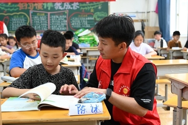 鄭州市二七區(qū)暑托班的志愿者輔導(dǎo)孩子寫作業(yè)。人民網(wǎng)記者王玉興攝