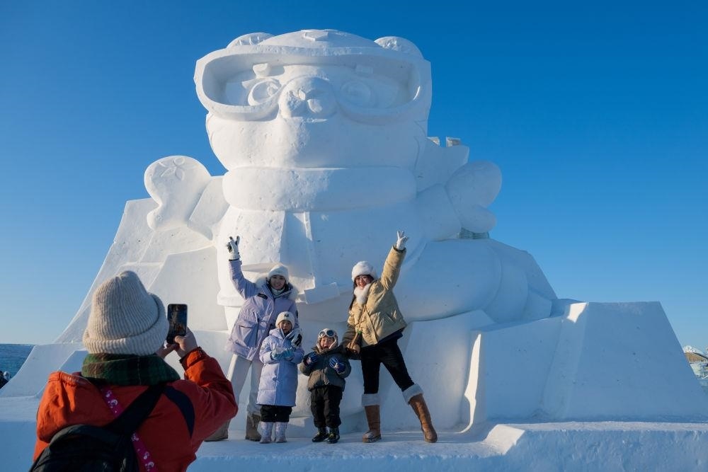 2025年1月3日，在黑龍江哈爾濱冰雪大世界園區(qū)，游客與亞冬會(huì)吉祥物雪雕“濱濱”合影